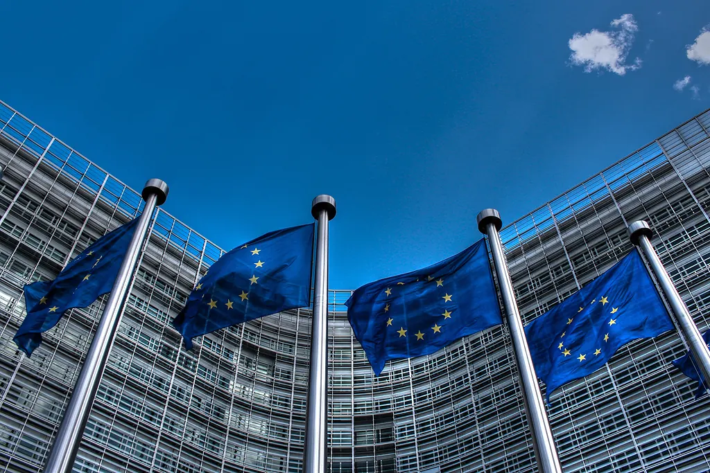 Brüksel'de Berlaymont binasının cam cephesi önünde mavi gökyüzü altında dalgalanan Avrupa Birliği bayrakları