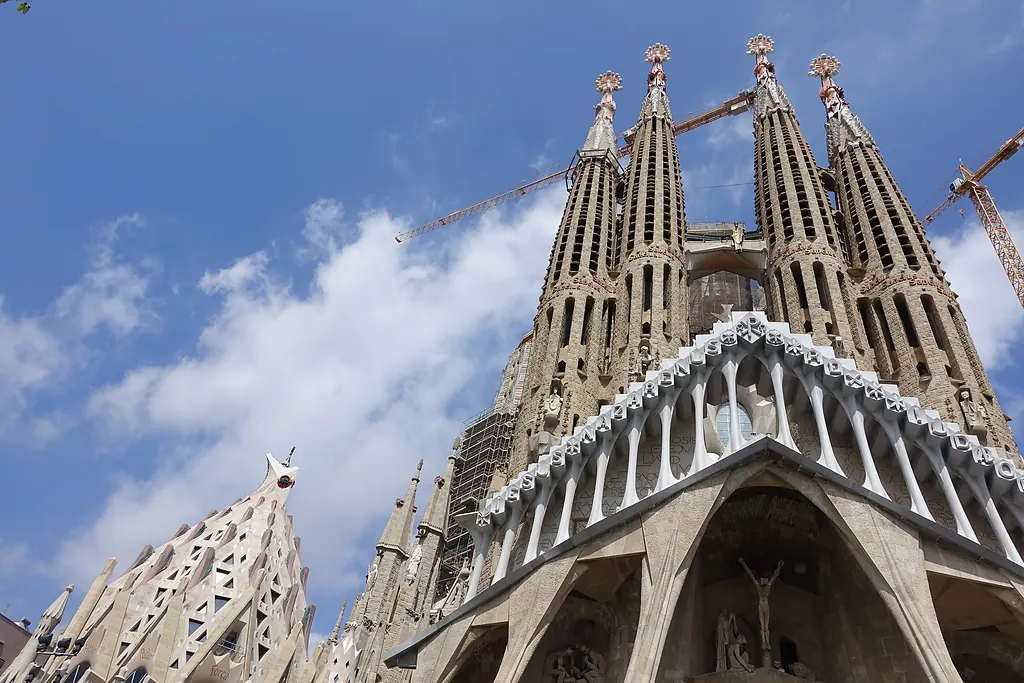 Sagrada Família'nın Tutku Cephesi ve üzerinde yükselen kuleler, bulutlu mavi gökyüzünde