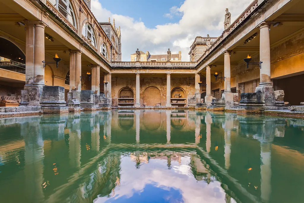 Bath'taki Roma Hamamları'nın Büyük Havuzu, yeşil su, sütunlu galeri ve suya yansıyan bulutlu gökyüzü
