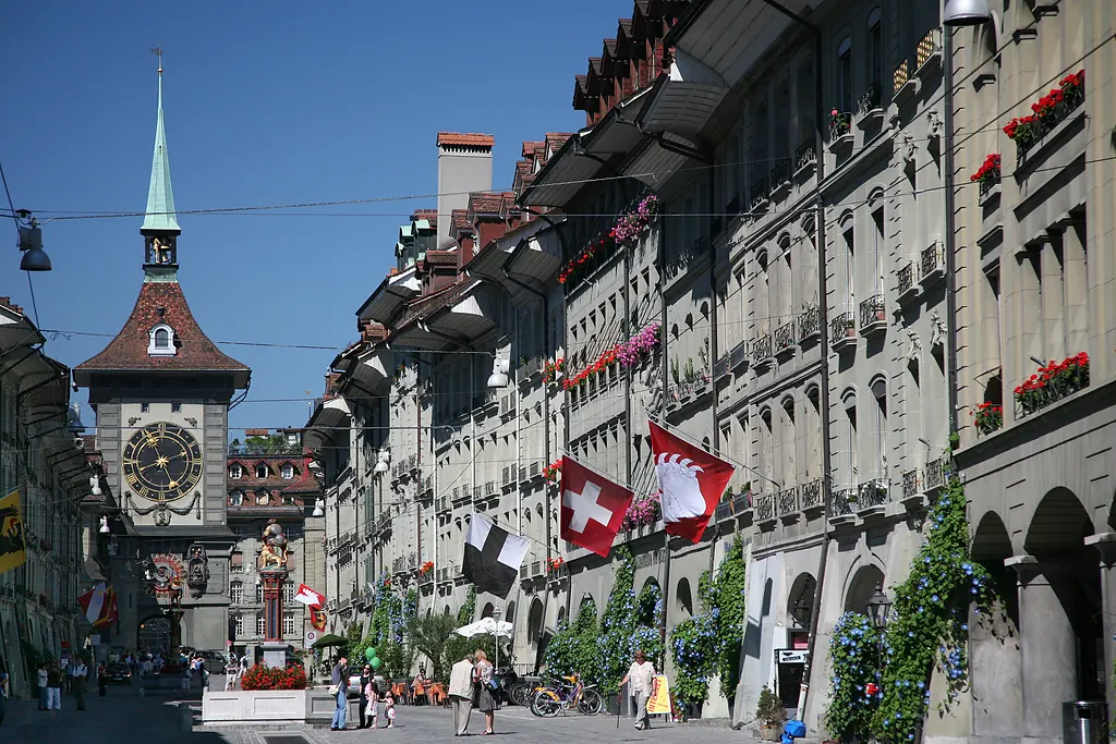 Bern eski şehrinde Kramgasse caddesi, soldaki Zytglogge saat kulesi ve sokağı süsleyen bayraklar