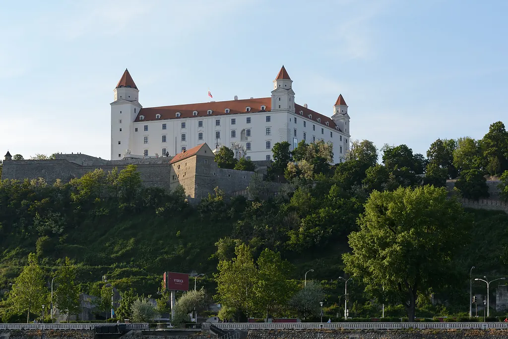 Bratislava Kalesi'nin beyaz ana yapısı ve köşe kuleleri, yamaçtaki yeşilliğin üzerinde