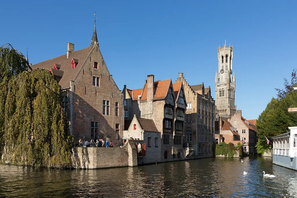 Brugge'de kanal kıyısındaki tuğla evler, solda salkım söğüt ve arkada yükselen Belfort çan kulesi