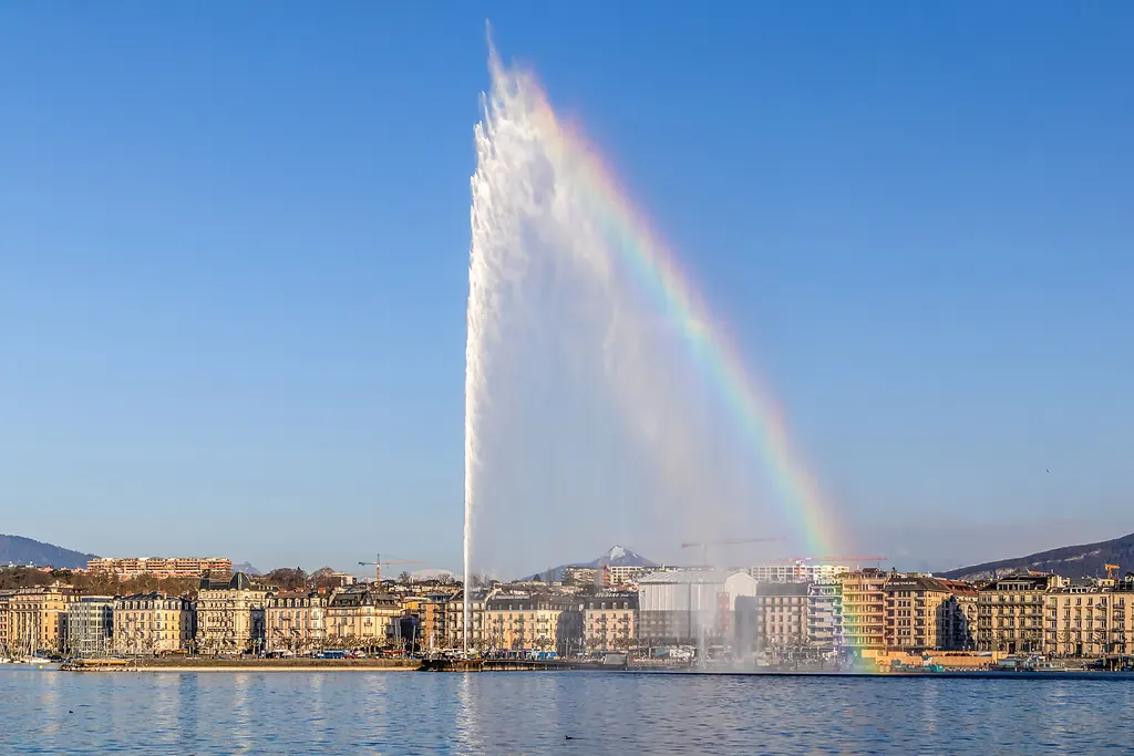Cenevre Gölü'nden fışkıran Jet d'Eau fıskiyesi ve üzerinde gökkuşağı, arkada şehir sahili