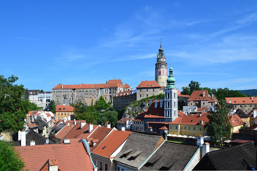 Çeski Krumlov'un kırmızı çatılı evleri ve kale kulesi, açık mavi gökyüzü altında