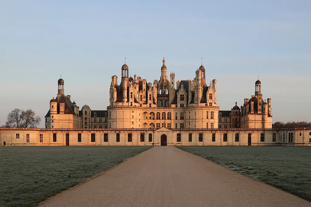 Gün doğumunda pembe ışıkla aydınlanan Chambord Şatosu ve önündeki çakıllı yol