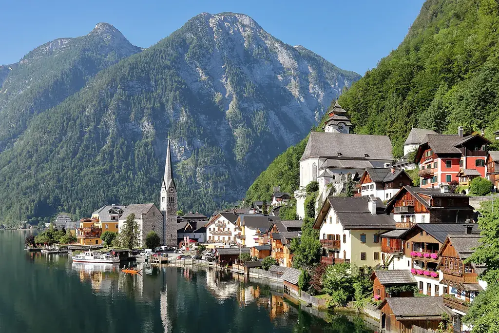 Hallstatt köyü; göl kıyısındaki ahşap evler, kilise kulesi ve arkada yükselen dağlar