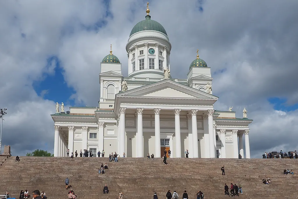 Helsinki Katedrali'nin beyaz cephesi ve yeşil kubbesi, önünde geniş taş merdivenler ve bulutlu gökyüzü