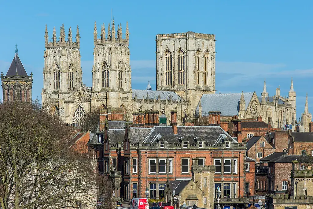 Kent surlarından York Minster Katedrali'nin üç kulesi, önünde kırmızı tuğlalı evler ve mavi gökyüzü